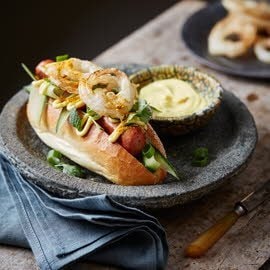 ''Haute dog'' met zoetzure komkommer, gefrituurde uienringen en Ras el hanut mayonaise