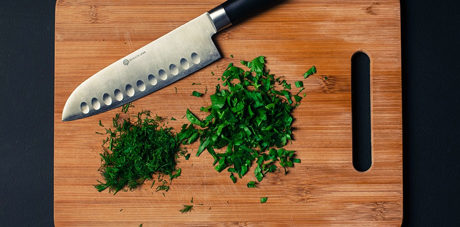 Houten snijplank met gesneden groene kruiden erop, met snijmes