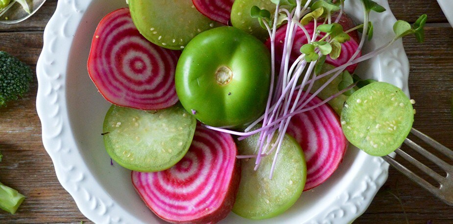 Schotel met felroze chioggiabieten, groene tomaatplakjes en kiemgroenten op een wit bord